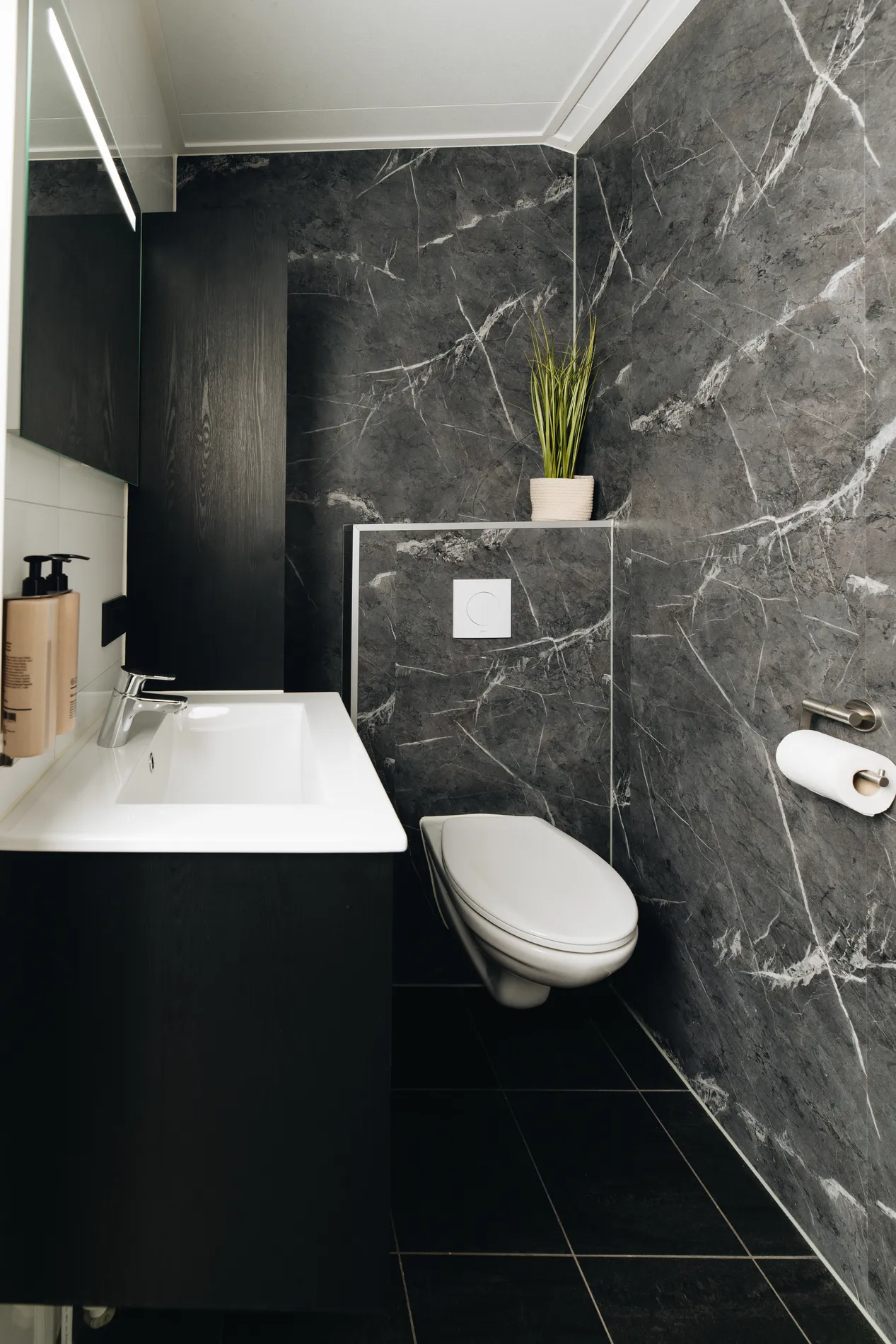 Luxe badkamer met donker marmeren wandafwerking, modern wit toilet en een strak wastafelmeubel.